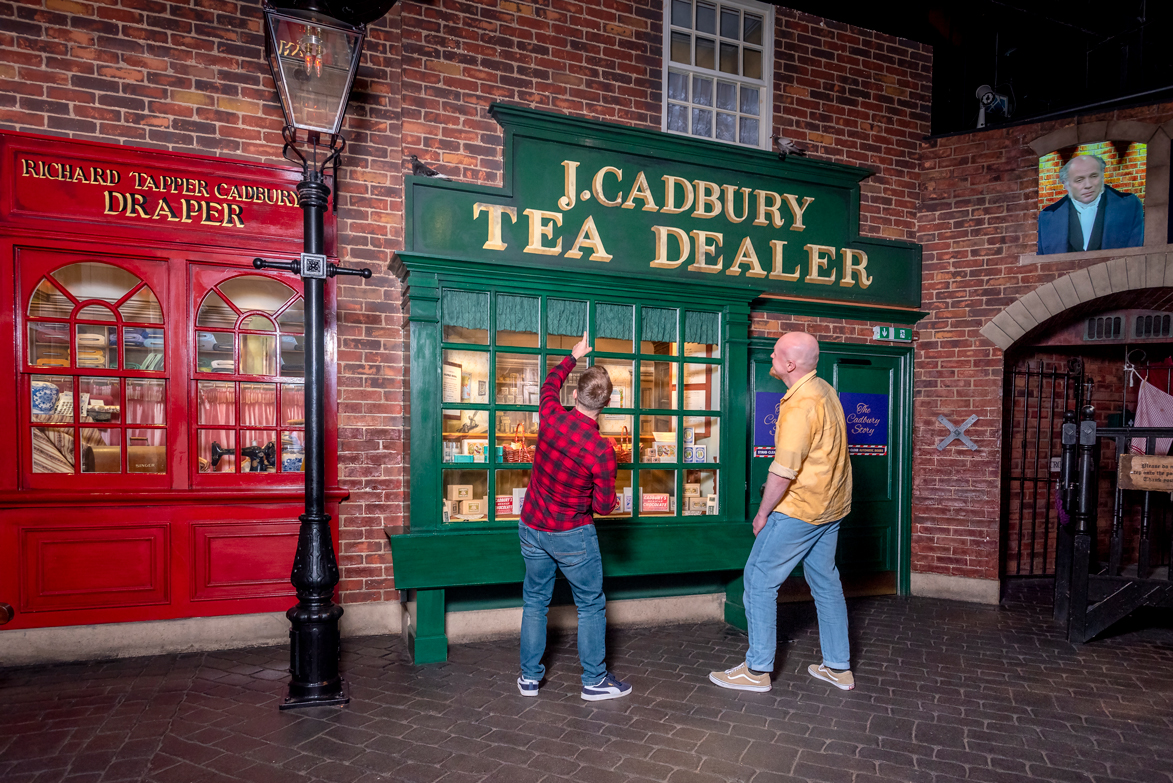 Two men pointing at the J. W Cadbury store front at Cadbury World