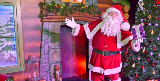 Santa in front of the fireplace holding a wrapped gift at Cadbury World